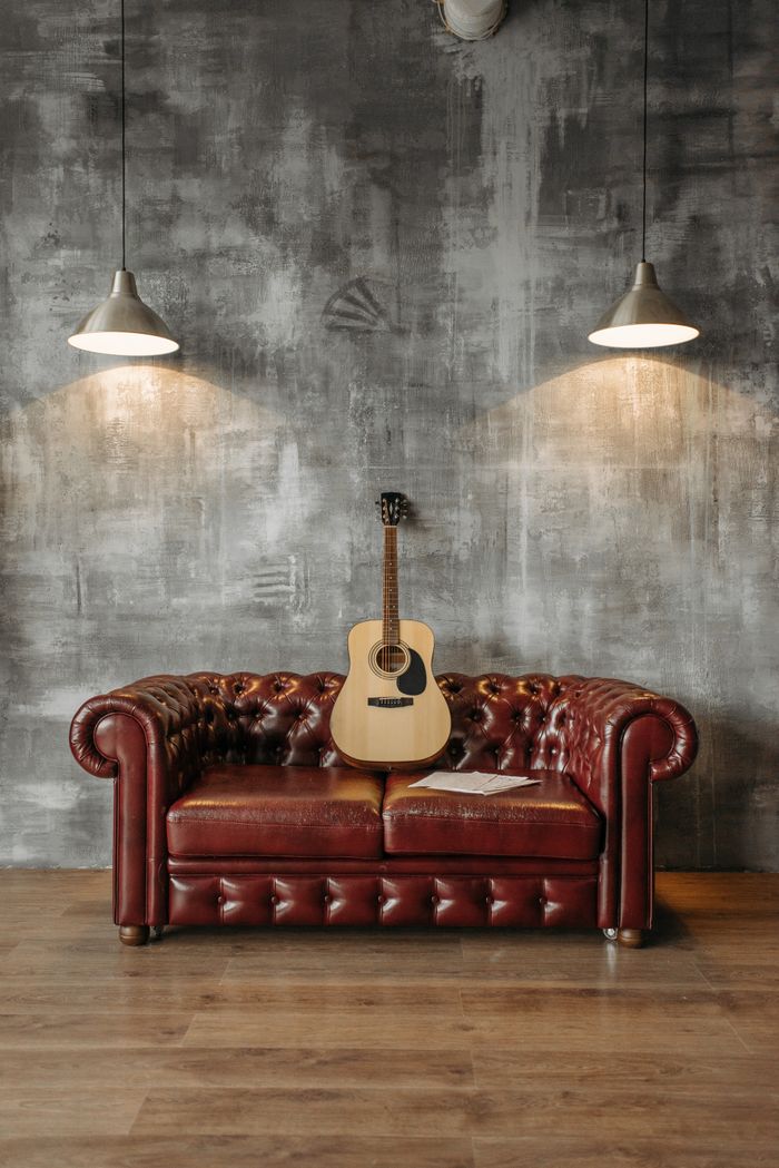 A cozy indoor setting with a leather couch, acoustic guitar, and hanging lamps in a rustic style.